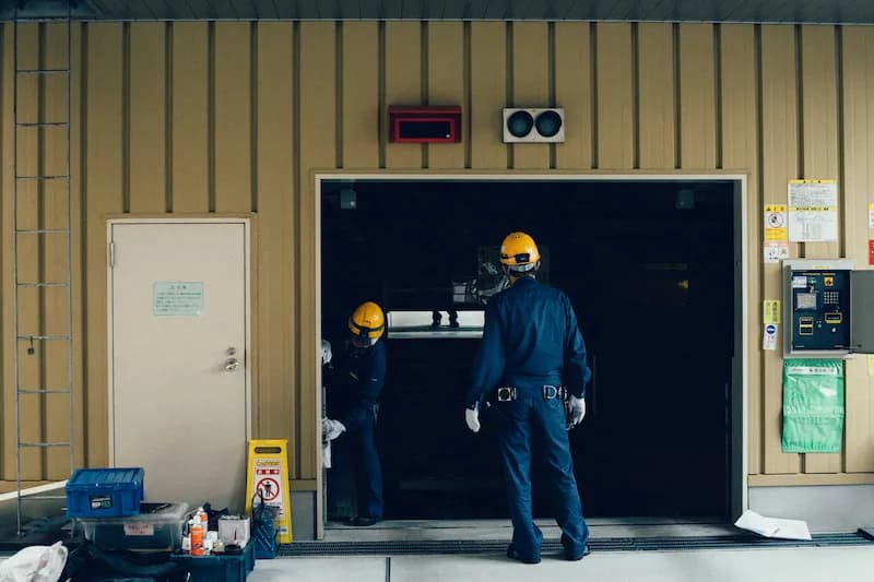 Two technicians in hard hats and work uniforms inspecting a building entrance